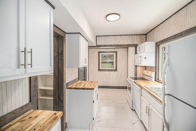 kitchen with butcher block countertops, sink, wooden walls, white appliances, and white cabinets