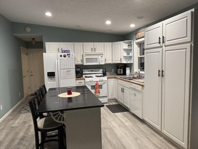 kitchen with vaulted ceiling, sink, white appliances, a kitchen breakfast bar, and white cabinets