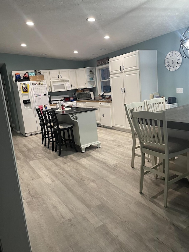 kitchen with light wood-type flooring, white cabinets, a breakfast bar, and white appliances