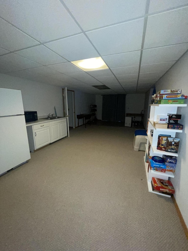 basement with sink, carpet, white refrigerator, and a paneled ceiling