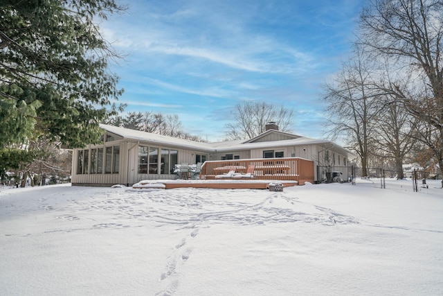 snow covered house with a wooden deck and a sunroom