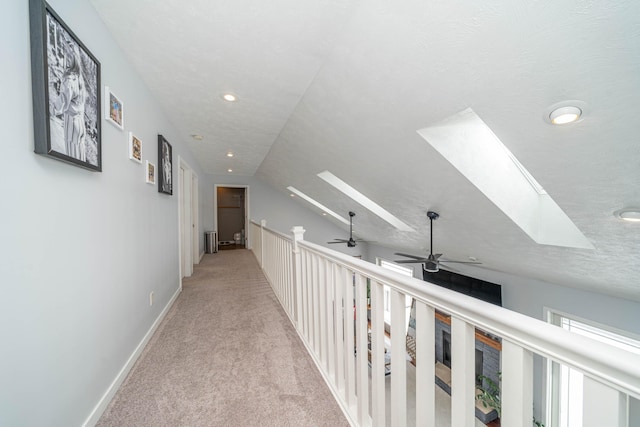 corridor featuring a textured ceiling, lofted ceiling with skylight, and light carpet