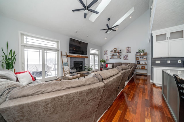 living room with dark hardwood / wood-style flooring, a skylight, a brick fireplace, ceiling fan, and high vaulted ceiling