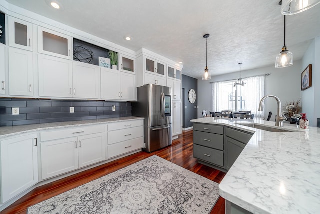 kitchen featuring white cabinetry, decorative backsplash, hanging light fixtures, stainless steel fridge, and a kitchen island with sink