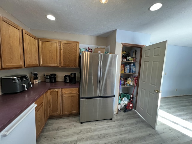 kitchen featuring a textured ceiling, dishwasher, light hardwood / wood-style flooring, and stainless steel refrigerator