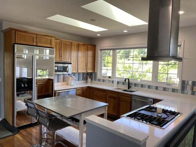 kitchen featuring a skylight, stainless steel appliances, sink, island range hood, and hardwood / wood-style flooring