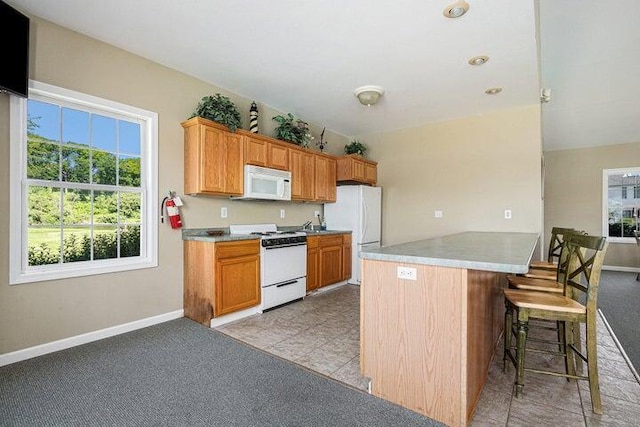 kitchen featuring a breakfast bar area, light colored carpet, kitchen peninsula, and white appliances