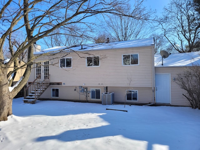 snow covered rear of property featuring central AC