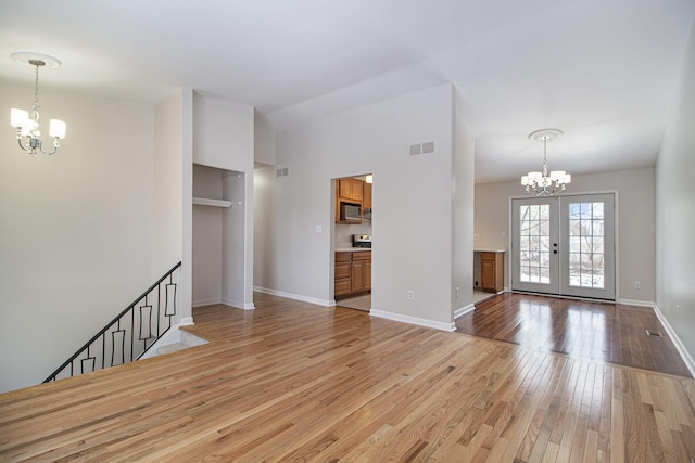 unfurnished living room with french doors, a chandelier, and light wood-type flooring