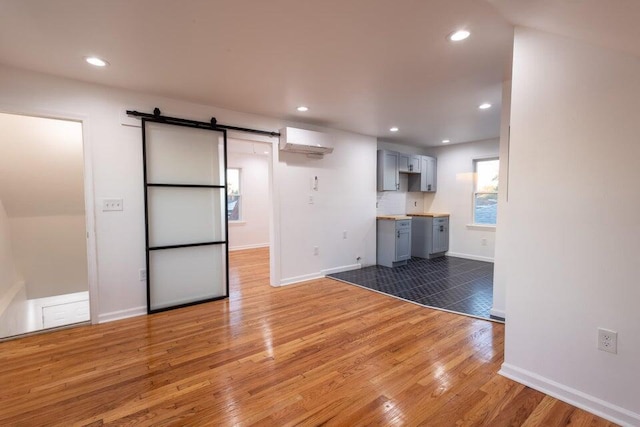 interior space with a barn door, a wall mounted AC, gray cabinetry, and wood-type flooring