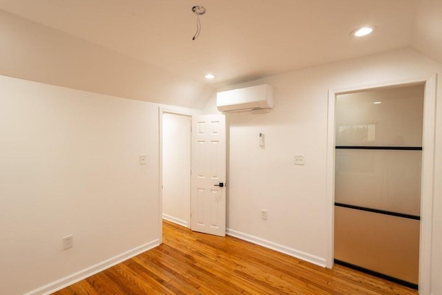 unfurnished room featuring lofted ceiling, a wall unit AC, and light wood-type flooring