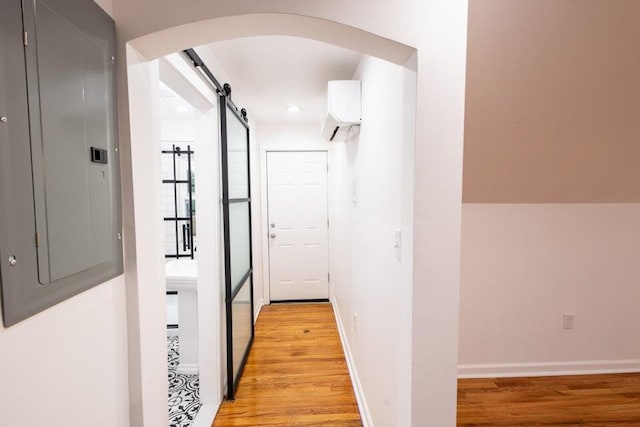 hallway with electric panel, a wall mounted AC, a barn door, and light hardwood / wood-style flooring