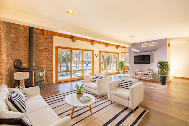 living room with beam ceiling, light wood-type flooring, and a wood stove