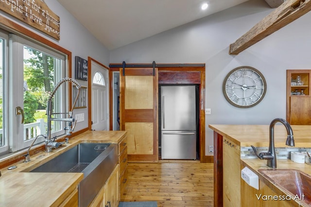 kitchen with vaulted ceiling, a barn door, sink, and stainless steel refrigerator