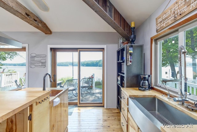 kitchen featuring sink, a water view, wooden counters, light hardwood / wood-style flooring, and beam ceiling