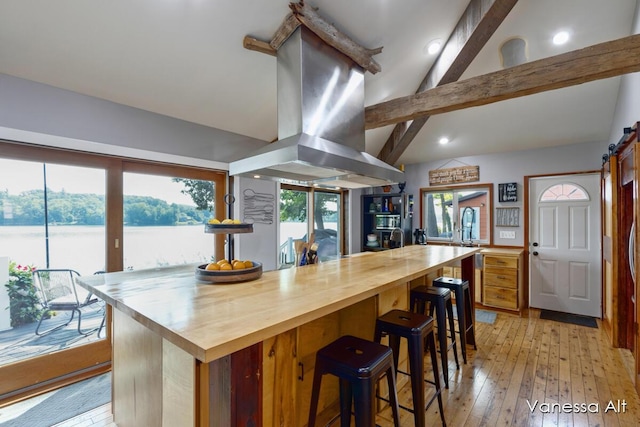 kitchen featuring butcher block countertops, vaulted ceiling with beams, island range hood, light wood-type flooring, and a barn door