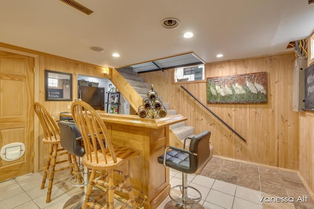 bar with light brown cabinetry, wooden walls, and light tile patterned flooring