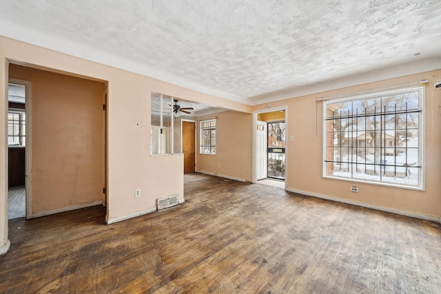 unfurnished living room with ceiling fan, dark hardwood / wood-style floors, a wealth of natural light, and a textured ceiling