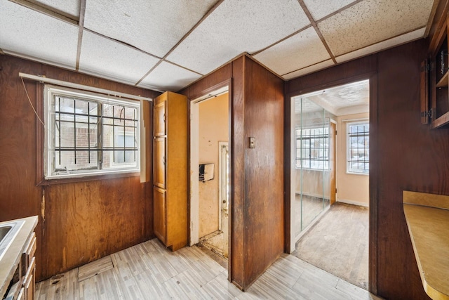 interior space featuring light hardwood / wood-style floors, a drop ceiling, and wooden walls