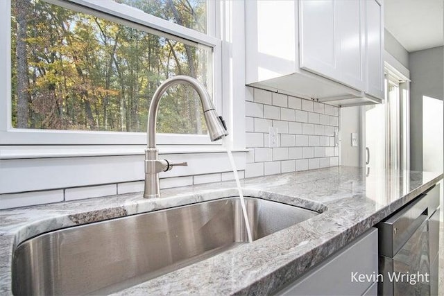 room details with white cabinetry, decorative backsplash, sink, light stone counters, and stainless steel dishwasher