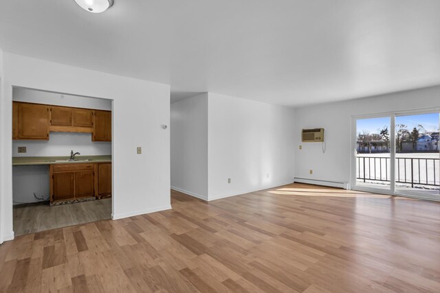 unfurnished living room with baseboards, a sink, light wood-type flooring, and a baseboard radiator
