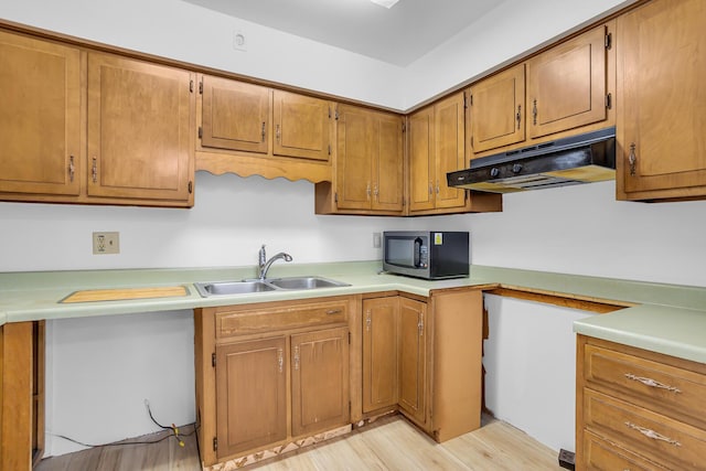 kitchen featuring light countertops, stainless steel microwave, under cabinet range hood, a sink, and brown cabinets