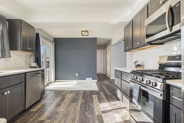 kitchen featuring dark brown cabinetry, decorative backsplash, dark wood-type flooring, and appliances with stainless steel finishes