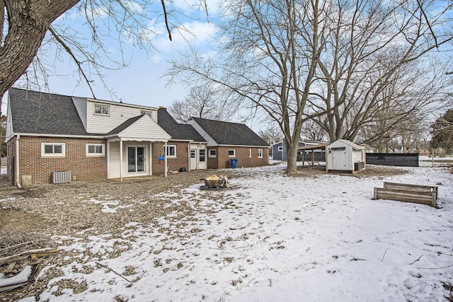 snow covered back of property featuring central AC and a shed