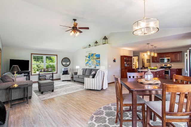 dining area featuring vaulted ceiling, ceiling fan with notable chandelier, and light hardwood / wood-style flooring