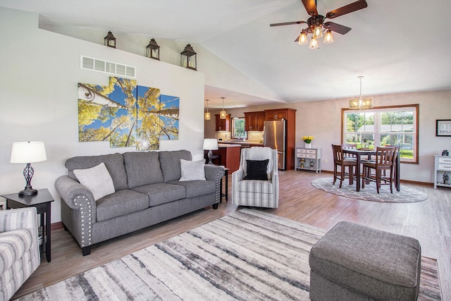 living room with ceiling fan with notable chandelier, light hardwood / wood-style flooring, and lofted ceiling