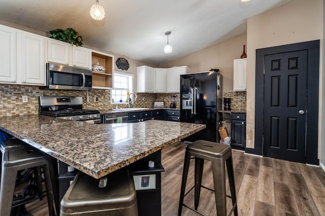 kitchen with stainless steel appliances, lofted ceiling, white cabinetry, and hanging light fixtures