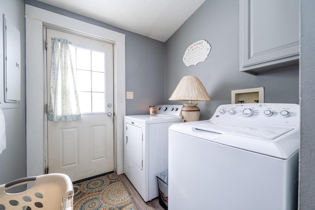 laundry area with light hardwood / wood-style flooring, washing machine and dryer, electric panel, and cabinets