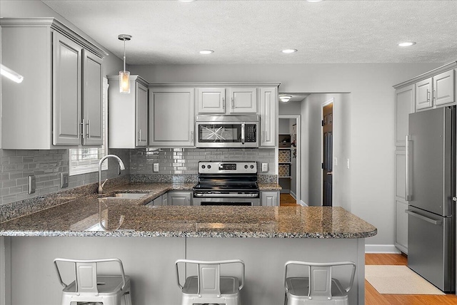 kitchen featuring appliances with stainless steel finishes, gray cabinetry, kitchen peninsula, and dark stone counters