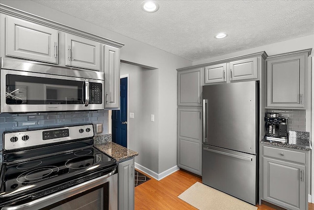 kitchen with stainless steel appliances, dark stone counters, backsplash, light wood-type flooring, and gray cabinetry