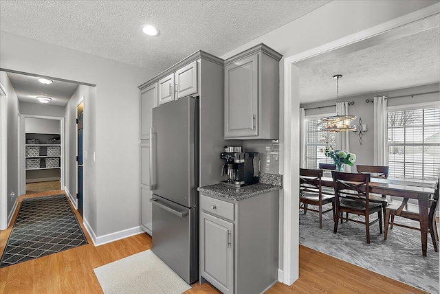 kitchen with a textured ceiling, stainless steel refrigerator, gray cabinets, and light hardwood / wood-style flooring