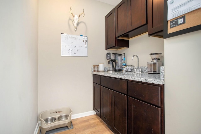 bar featuring light stone countertops, sink, dark brown cabinets, and light wood-type flooring