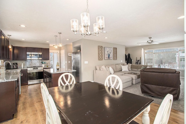 dining area with sink, ceiling fan with notable chandelier, and light hardwood / wood-style floors