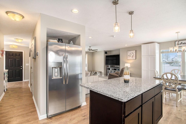 kitchen featuring pendant lighting, dark brown cabinetry, stainless steel fridge, light stone counters, and light hardwood / wood-style flooring