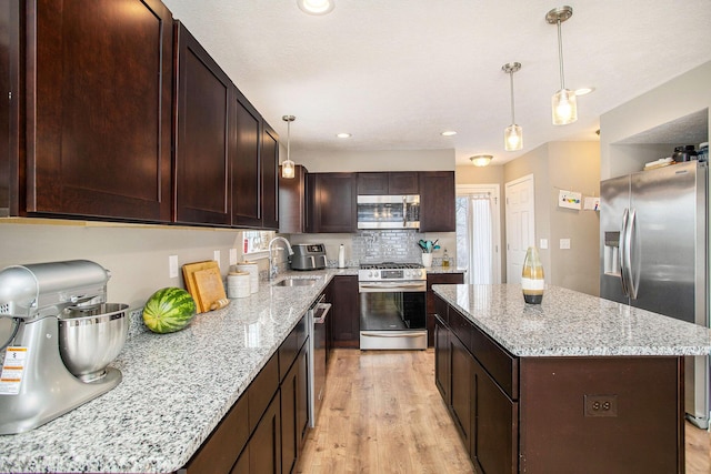 kitchen featuring light wood-type flooring, appliances with stainless steel finishes, a kitchen island, and sink