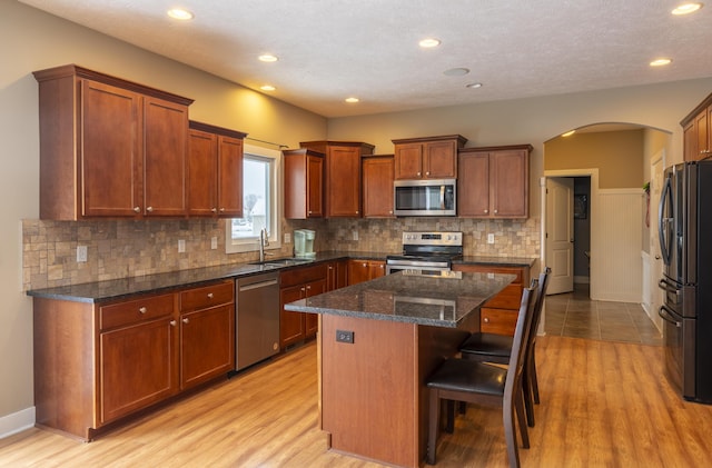 kitchen with appliances with stainless steel finishes, a center island, a kitchen bar, dark stone countertops, and sink