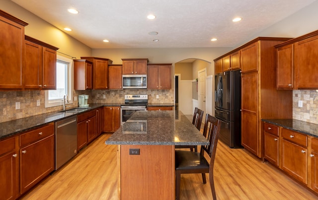 kitchen with a breakfast bar area, appliances with stainless steel finishes, a center island, dark stone counters, and sink