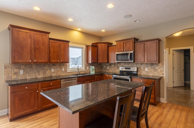 kitchen with dark stone countertops, light hardwood / wood-style floors, a center island, a kitchen breakfast bar, and stainless steel appliances