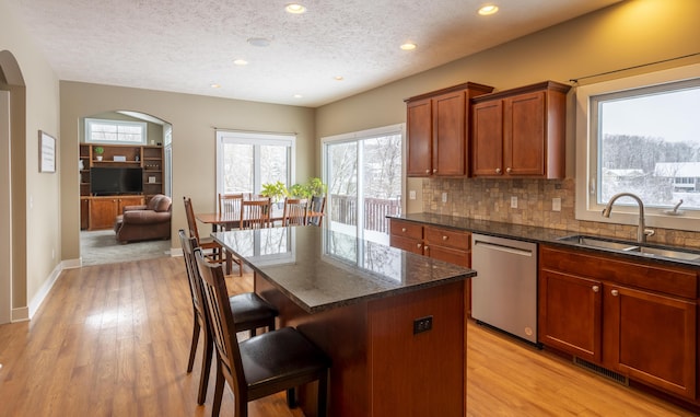 kitchen with a center island, a textured ceiling, stainless steel dishwasher, a breakfast bar, and sink