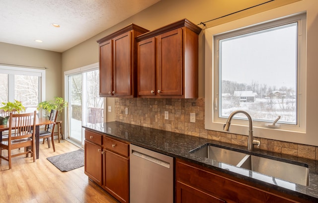 kitchen with a textured ceiling, dark stone counters, sink, stainless steel dishwasher, and light hardwood / wood-style flooring