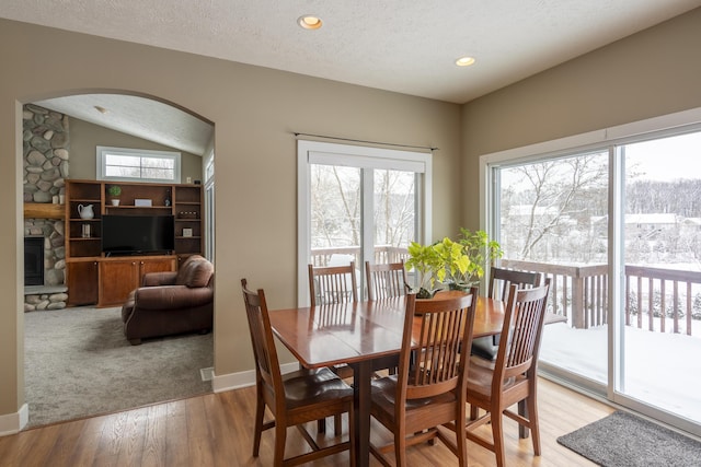 dining area featuring a textured ceiling, a fireplace, a healthy amount of sunlight, and light hardwood / wood-style floors