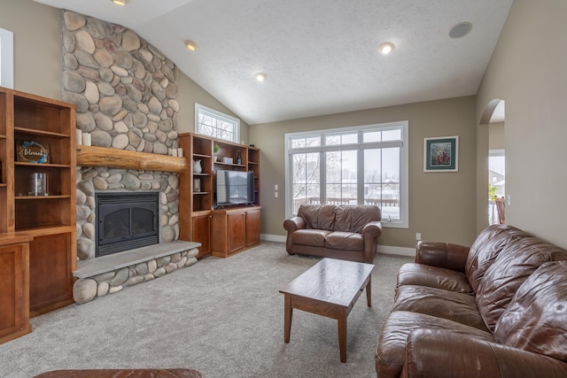 carpeted living room with a textured ceiling, lofted ceiling, and a stone fireplace