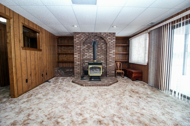 unfurnished living room featuring built in shelves, wood walls, carpet flooring, and a wood stove