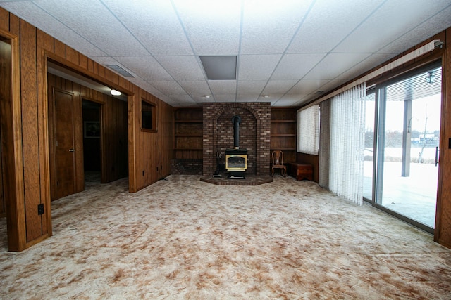 unfurnished living room with built in shelves, wood walls, light carpet, and a wood stove