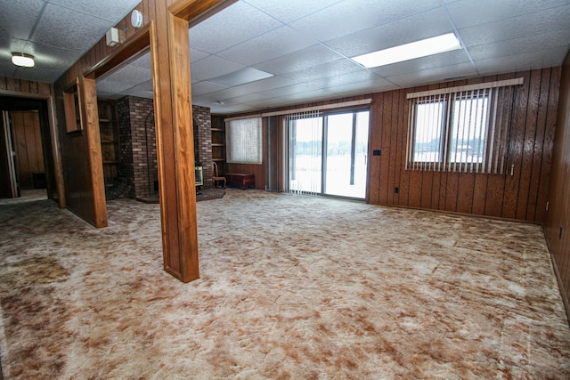 unfurnished living room with wood walls, a drop ceiling, brick wall, and carpet