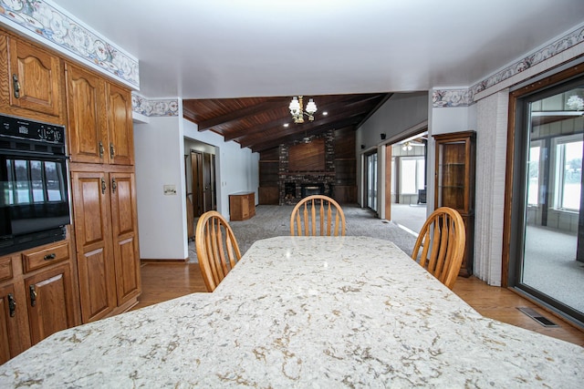 dining room with a brick fireplace, light colored carpet, and wooden ceiling